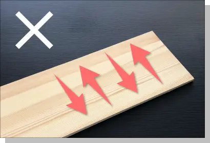 誤ったサンディングの方向を示す解説写真。木目を垂直に横切るように赤い矢印が動いており、仕上がりに傷が残ってしまう悪い例。